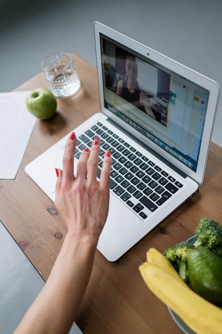 A woman in a video call on a laptop with fruits and vegetables on a wooden table.